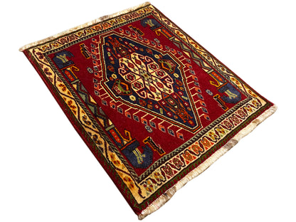 Poshti-tapijt (59×61 cm) diagonaal uitgespreid, rood geometrisch patroon met franjes