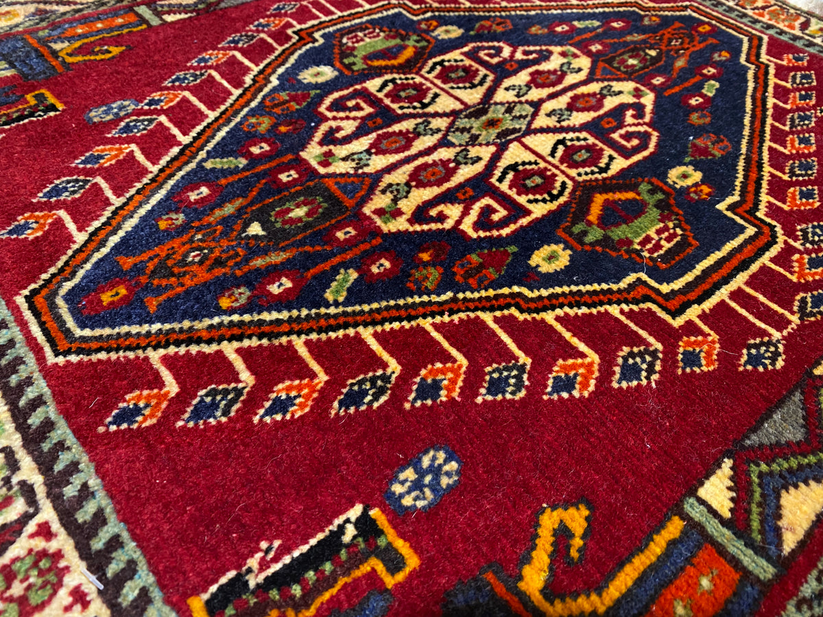 Close-up van een Poshti-tapijt (59×61 cm): rood binnenpatroon met kleurrijke ornamenten en rand