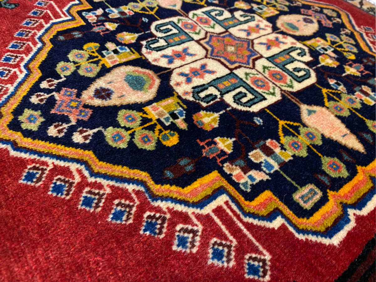 Poshti-tapijt met donkerblauw midden, rode randen en kleurrijke geometrische motieven
