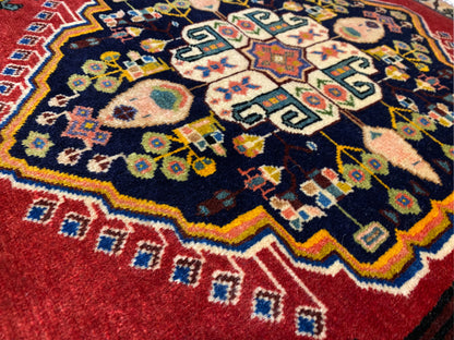 Poshti-tapijt met donkerblauw midden, rode randen en kleurrijke geometrische motieven