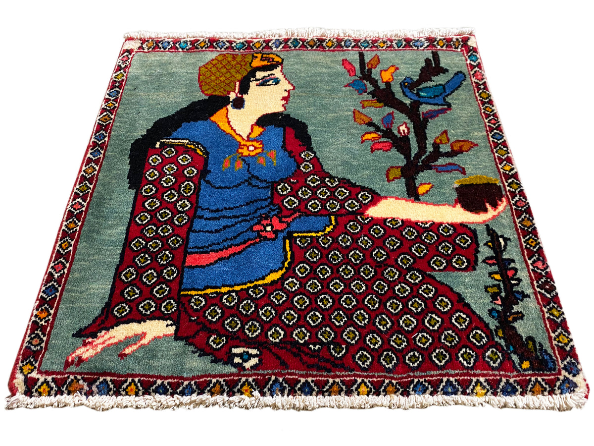 Poshti-tapijt 68x63 cm in driekwartaanzicht met figuur, boom, rode patroonranden, franjes