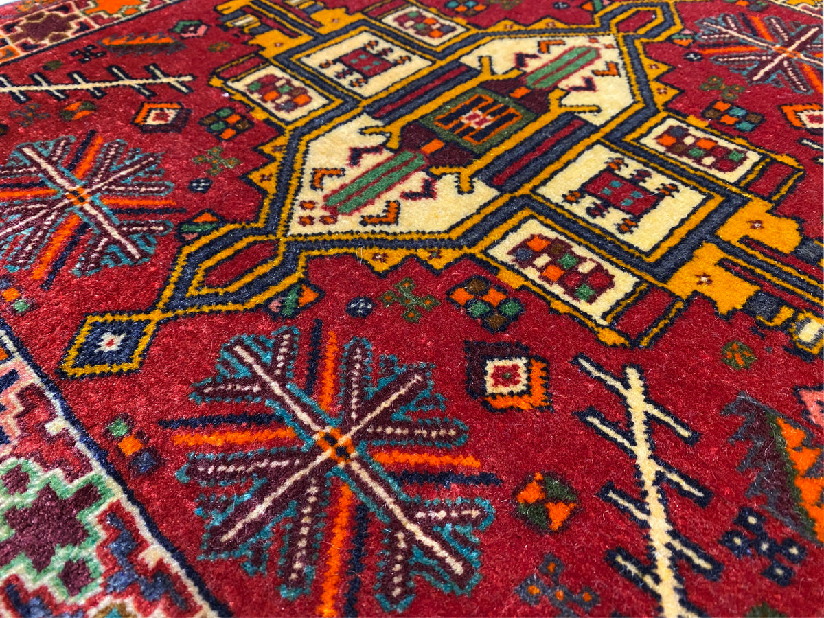 Close-up: Poshti-tapijt met rode achtergrond en kleurrijke geometrische motieven