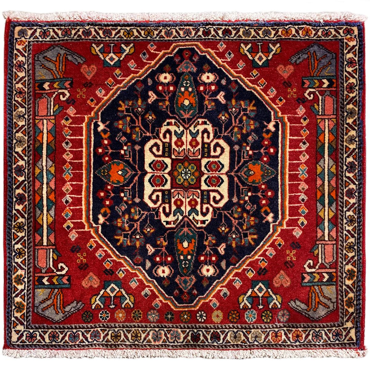 Vierkant tapijt met rode achtergrond en donkerblauw centraal motief, met franjes