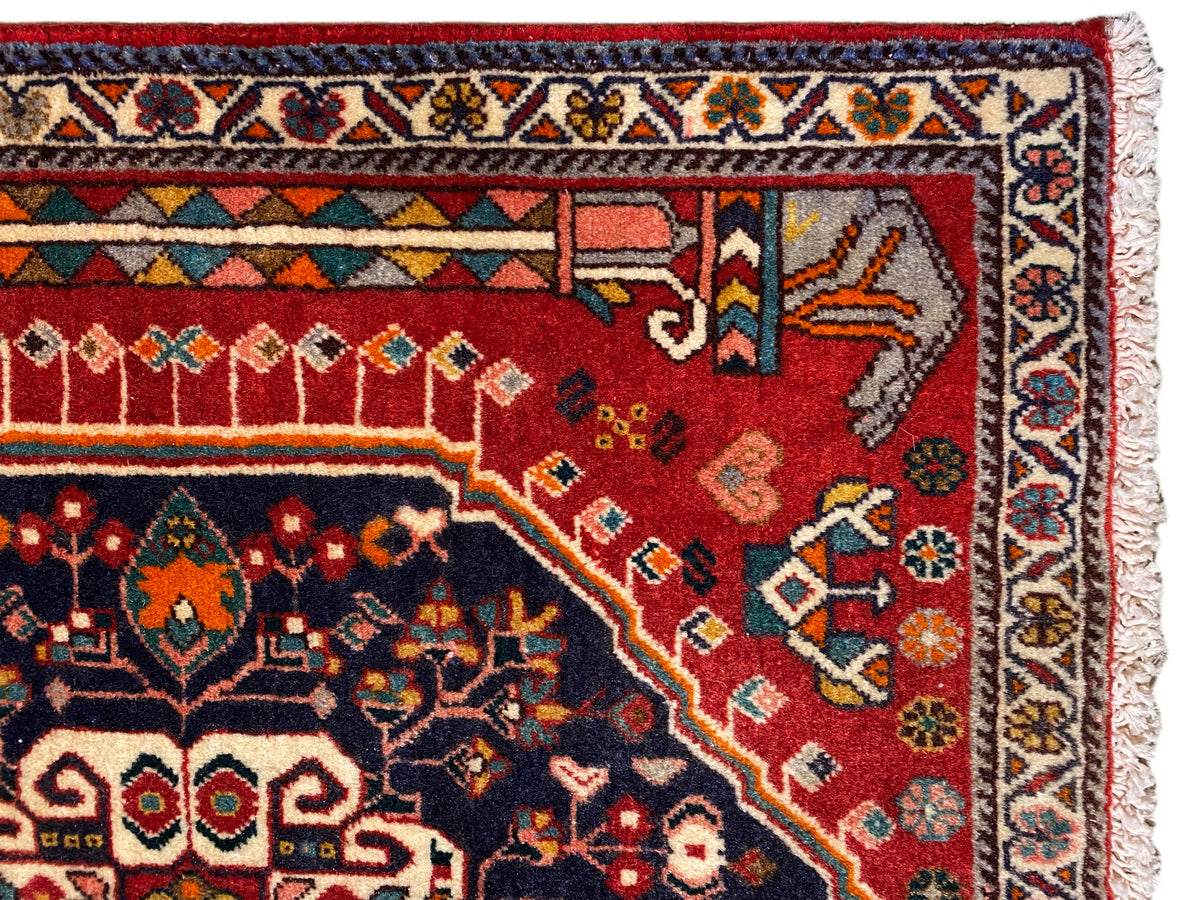 Tapijndetail: rood en blauw ornamentvlak met veelkleurige rand en franjes