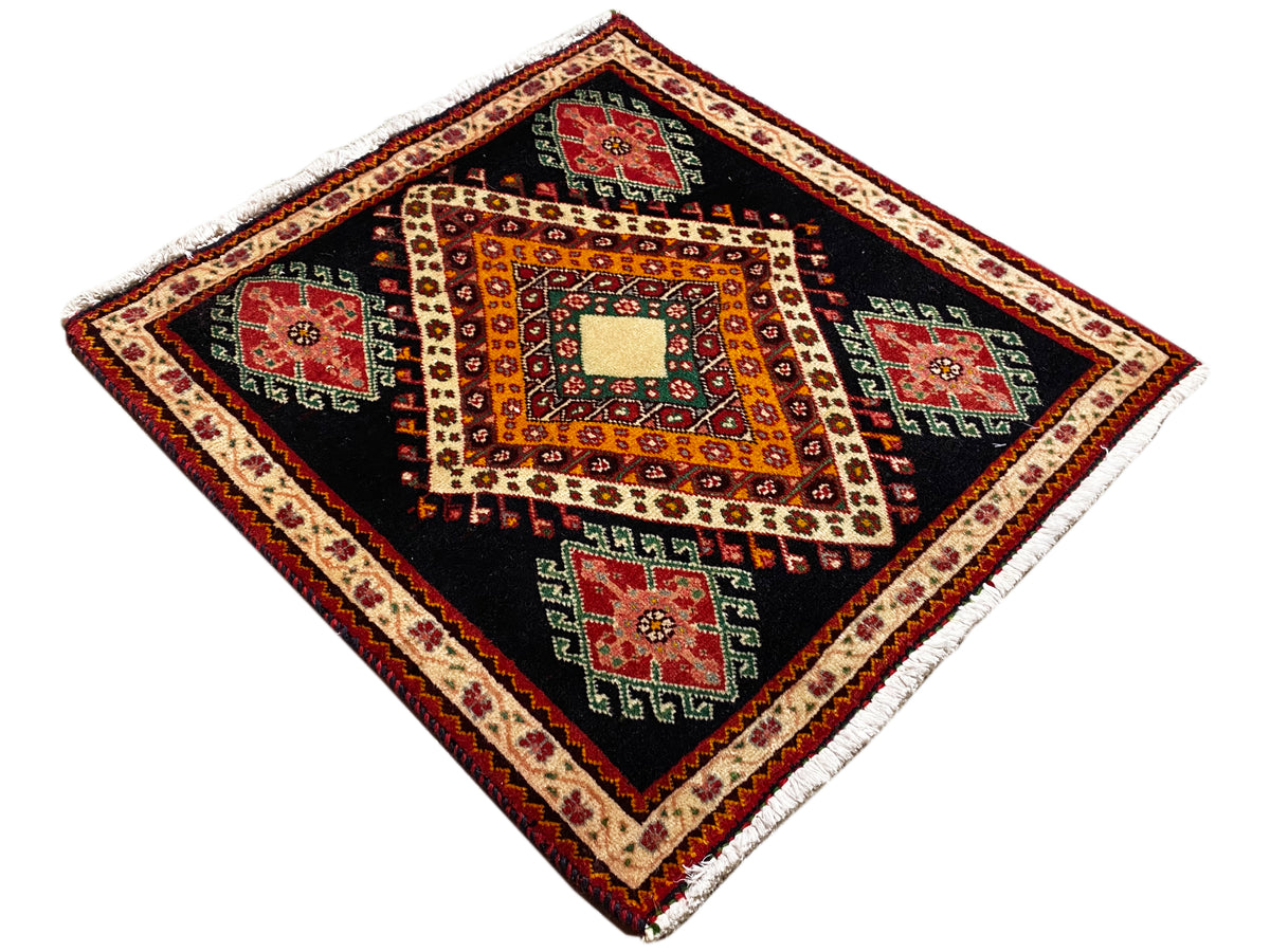 Poshti-tapijt uitgespreid in diamantweergave: zwarte basis, oranje patronen en rode/groene vlakken