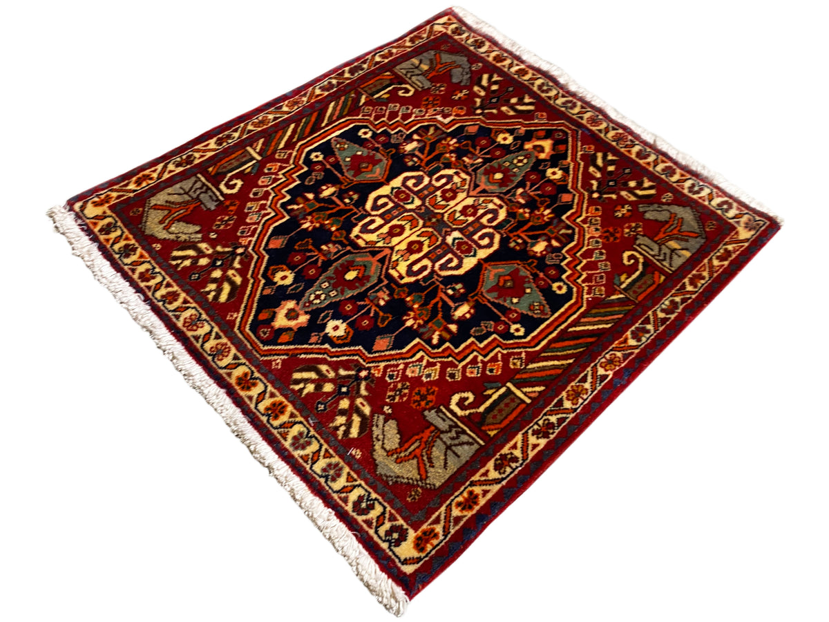 Tapijt 65x59 cm met een rode achtergrond, donkere middenornamenten en franjes aan de randen