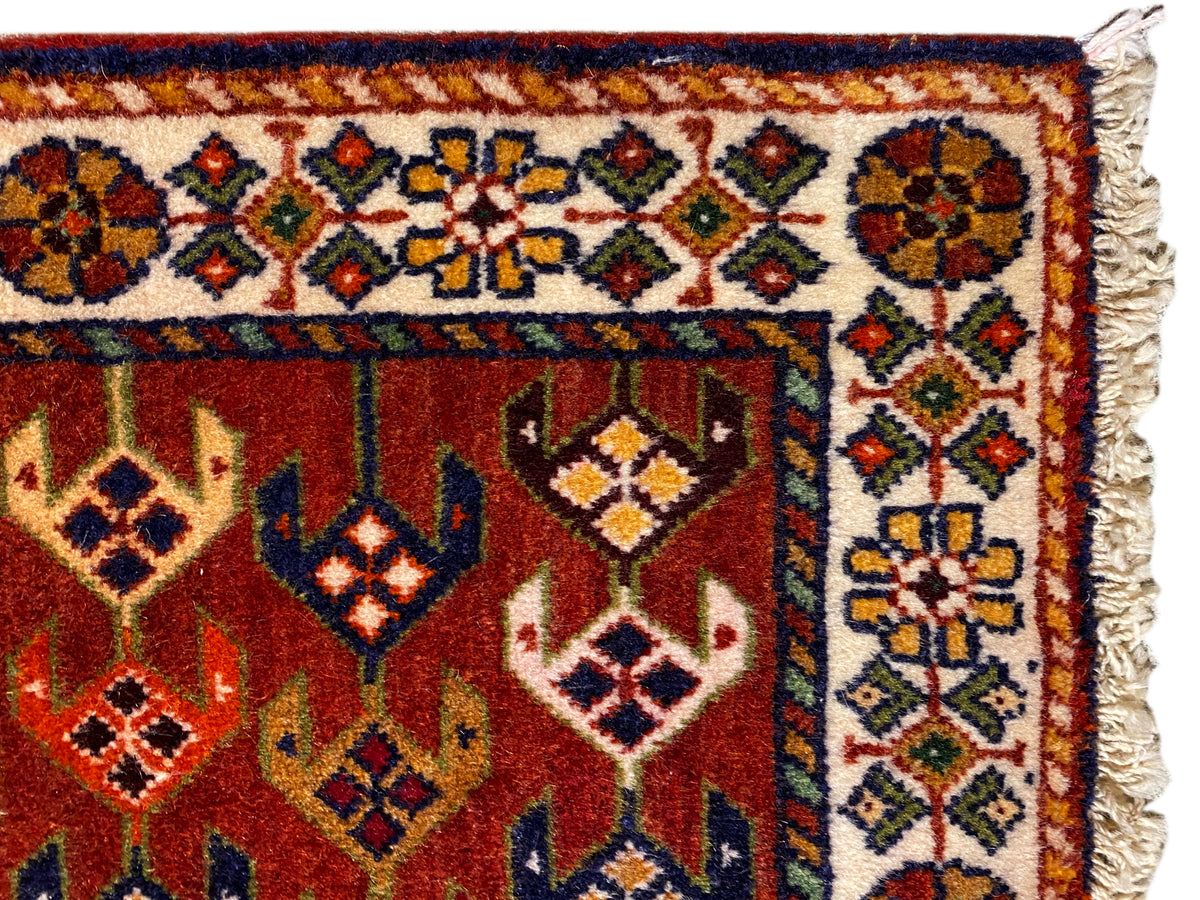 Tapijndetail: rood oppervlak met sierboord, kleurrijke ruiten en uitgerafelde zijkanten