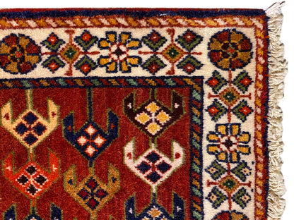 Tapijndetail: rood oppervlak met sierboord, kleurrijke ruiten en uitgerafelde zijkanten