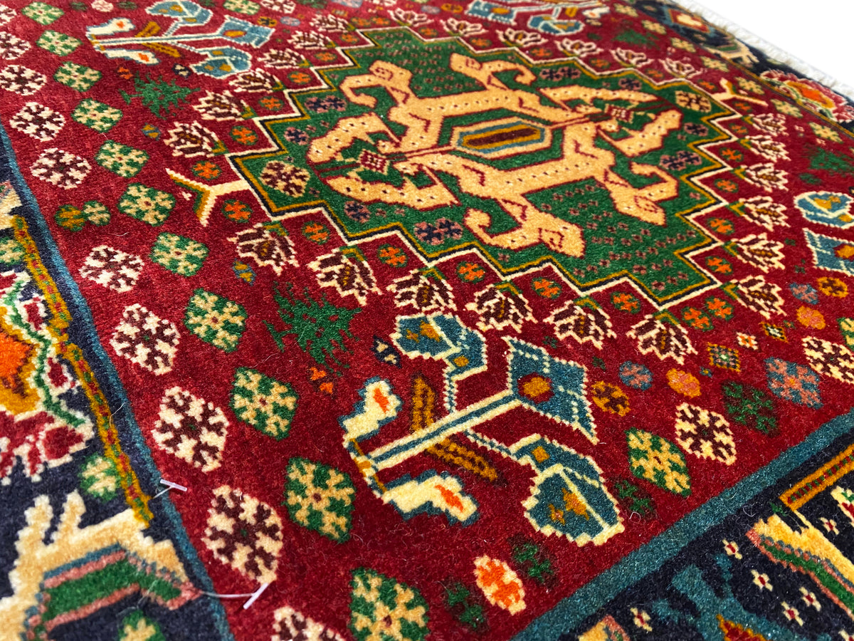 Detail van de voorkant van een tapijt met een rood vlak, stervormige patronen en turquoise lijnen, gestructureerde pool