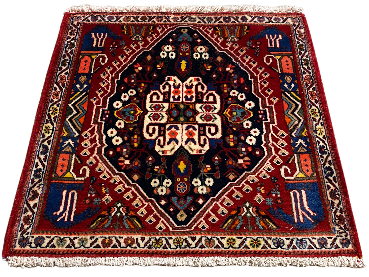 Tapijt met rode rand, donkerblauw midden en veelkleurige ornamenten, franjes