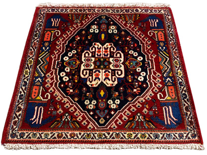 Tapijt met rode rand, donkerblauw midden en veelkleurige ornamenten, franjes