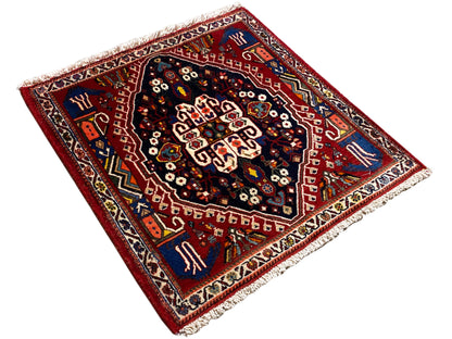 Vierkant ogend tapijt met een rode basis, donkerblauw centraal medaillon en franjes